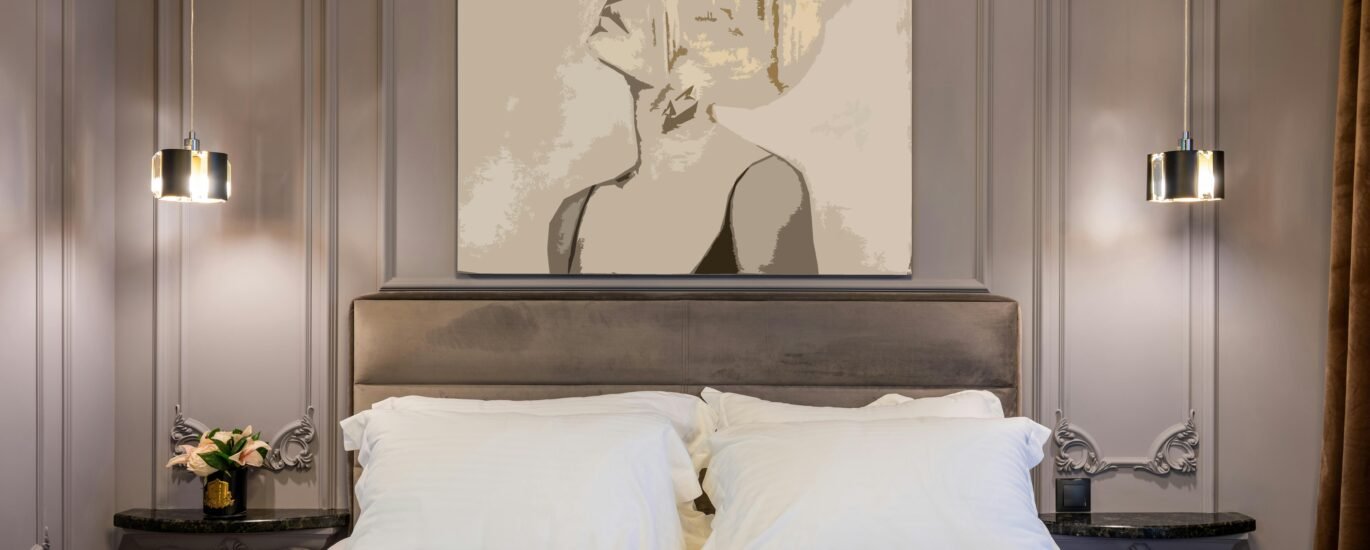 Contemporary bedroom with pillows and cover on bed between tables with flower bouquet under shiny lamp in house